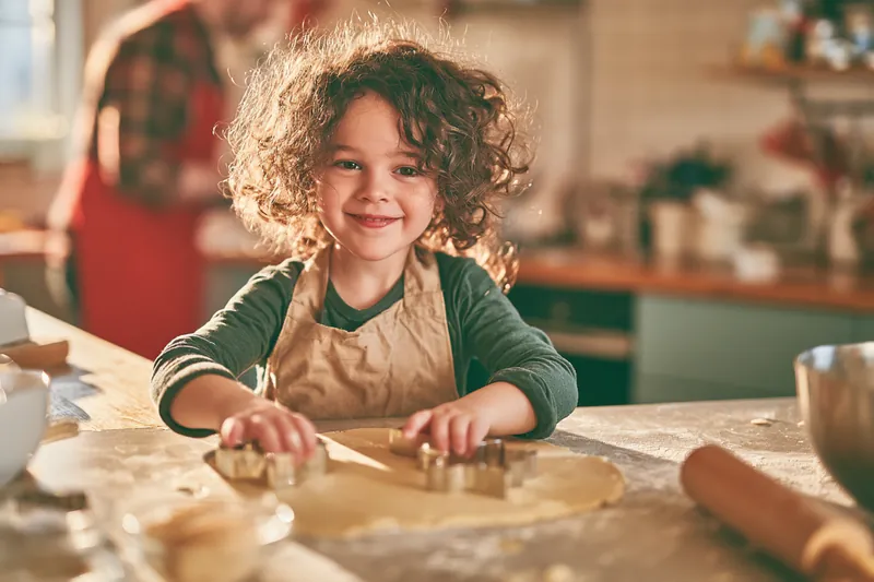Family baking holiday cookies together at home, a child pressing cookie cutters into dough, an affordable tradition that protects the money stash