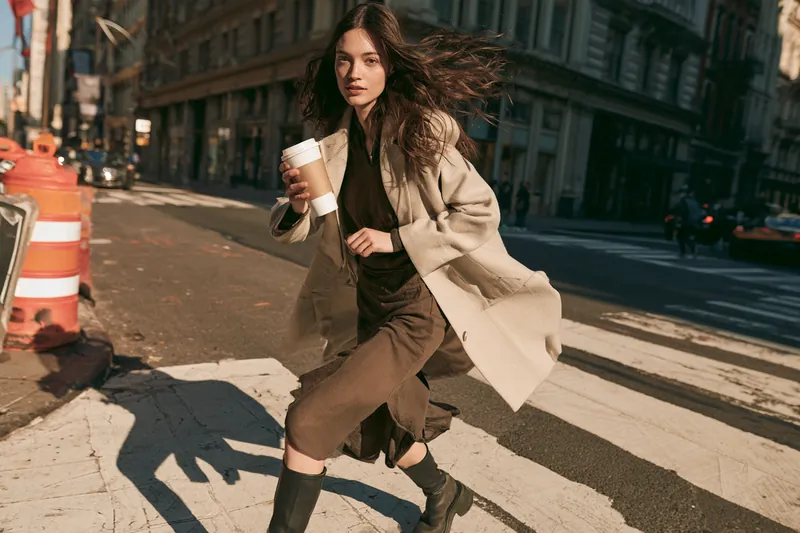 Young woman dashing across a city crosswalk with a takeaway coffee, racing a deadline after her money stash ran out