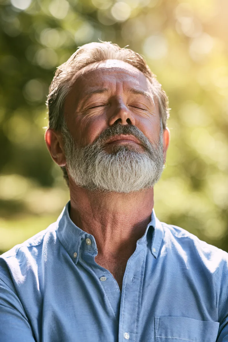 Man in his sixties breathing in fresh air on a sunny park path, relaxed after sorting out his medical bill